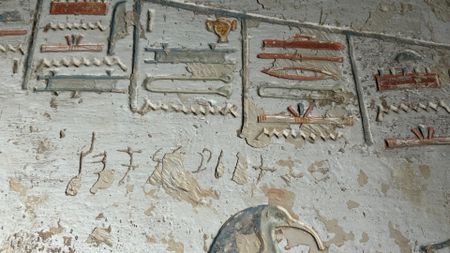 A white wall shows golden and blue heiroglyphs along with small letters carved into the wall
