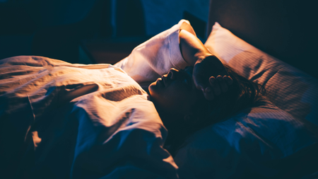 Woman with Insomnia. Young woman lying on bed with hand on forehead.